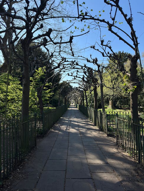 A well-maintained garden featuring lush green grass and neatly edged flower beds filled with vibrant pink, purple, and white flowers. A paved pathway curves through the garden, bordered by colorful pl